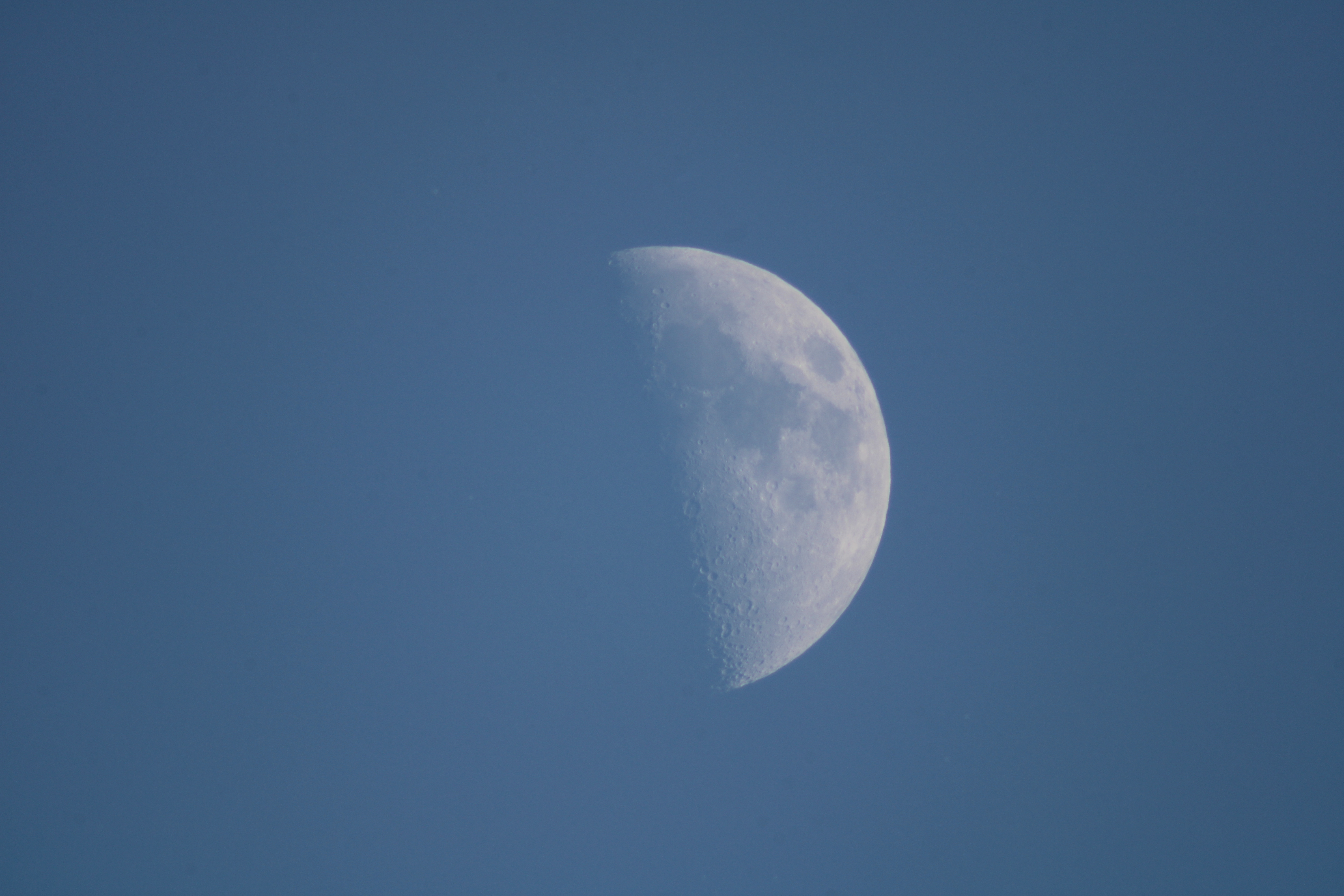 A detailed photo of a half moon taken during the day